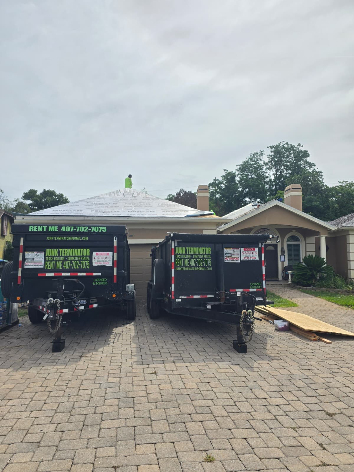 Two Junk Terminator dumpsters standing side by side in front of a home